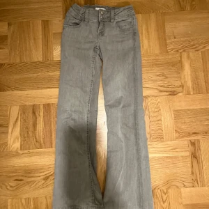 Grå jeansbyxor från Gina Tricot - Snygga grå jeansbyxor från Gina Tricot med bootcut-stil. Byxorna har en klassisk design med två knappar i midjan och är perfekta för en avslappnad look. De är tillverkade i ett bekvämt material som passar bra till vardags.
