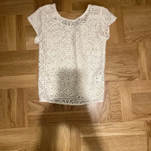 Vit spetsblus - Säljer en söt vit spetsblus med korta ärmar. Perfekt för varma dagar och ger en romantisk touch till din outfit. Blusen har ett vackert mönster och är lätt att matcha med olika stilar.