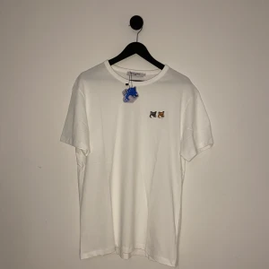 Maison Kitsune T-shirt - Vit t-shirt från Maison Kitsuné med två broderade rävmotiv på bröstet. T-shirten har en klassisk rund hals och korta ärmar. Perfekt för en stilren och avslappnad look. Helt ny med tags på, storlek L men små i storlek så passar S-M.