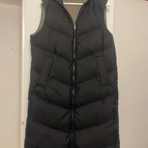 Zara väst - Snygg och lång väst från Zara. Jackan är svart på utsidan och har en grön/grå färg på insidan.