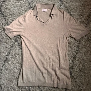 Beige pikétröja från A Day's March - Säljer en stilren beige pikétröja från A Day's March. Tröjan har korta ärmar och en klassisk krage, perfekt för en avslappnad men ändå snygg look. Passar bra till både jeans och chinos.