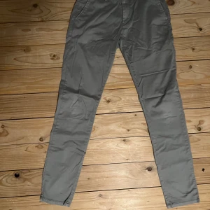 Grå chinos från SMOG - Snygga grå chinos från SMOG med normal passform. Byxorna har en klassisk design med knappar och dragkedja framtill. Perfekta för en stilren look. Kan jämföras med storlek S-M