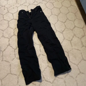 Svarta byxor med dragkedja - Säljer ett par svarta byxor med dragkedja och knappar. Perfekta för en casual look med en loose passform. + högmidjade