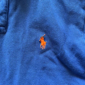 Blå pikétröja från Ralph Lauren - Säljer en snygg blå pikétröja från Ralph Lauren med den klassiska loggan broderad i orange på bröstet. Tröjan har korta ärmar och en stilren krage med knappar. Perfekt för både vardag och lite finare tillfällen!