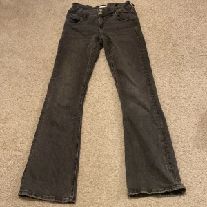 Svarta jeans med knappar - Säljer ett par svarta jeans i bra skick. De har en klassisk femficksdesign med snygga knappar både fram och bak. Jeansen har en Bootcut passform. De har även ett resårband runt midjan! 