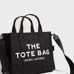 Väska - Helt ny Marc jacobs väska som jag inte använt alls, helt ren och oskadd. Passar så fint till vardags finns mycket utrymme också. Svart, canvas-tote i bomull från Marc Jacobs. Vit, tryckt logotyp fram och liten patch med logotyp på baksidan. Stängs me