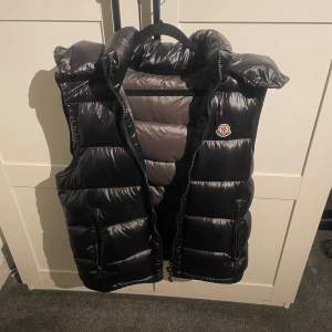 Säljer en snygg svart dunväst från Moncler. Västen har en glansig finish och är perfekt för kyligare dagar. Perfekt för höst, tags finns och nfc funkar. Storlekn är Y-S vilket passar storlek EU S alldeles utmärkt.