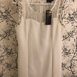 Kort Vit klänning  - Kort Vit klänning oanvänd prislappen på. Den är  knälång med pärlor på axlarna 
