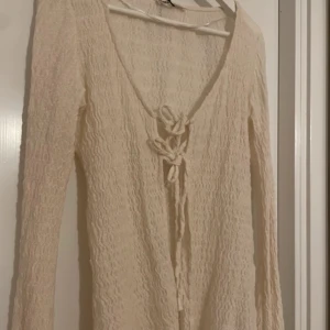 Beige långärmad kofta med knyt - Säljer en stilren beige kofta med lång ärm och knyt framtill. Koftan har en ribbad struktur som ger en fin textur och är perfekt för lager-på-lager-stil. Passar bra till både vardag och mer uppklädda tillfällen.