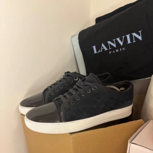 Lanvins uk8 - Snygga svarta sneakers från Lanvin i mocka med glansiga detaljer på tån och hälen. Skorna har en vit sula och klassisk snörning. Perfekta för en stilren look. Endast dustbag tillkommer vid köp priset går att diskutera vid snabb affär.