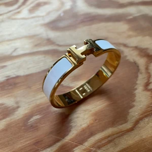 Guldarmband med vit emalj - Elegant guldarmband med vit emalj och ett stilrent H-format spänne. Perfekt för att ge en lyxig touch till din outfit. Armbandet har en slät och glänsande yta som fångar ljuset vackert. Plick låter inte mig ladda upp annonsen med märkets namn i titeln? Så skriv gärna i DM om ni har några frågor, kvitto finns 😁🌟