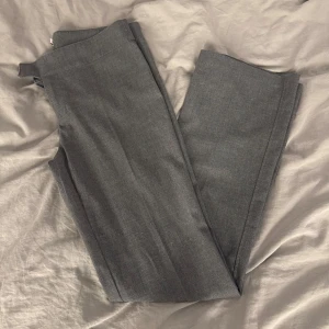 Grå kostymbyxor - Snygga grå kostymbyxor med en klassisk straight passform. De är lågmidjade och perfekta för en stilren look. Kostymbyxorna har ingen ficka vilket gör det cleant. 