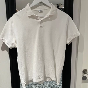 Vit pikétröja från East West - Säljer en klassisk vit pikétröja från East West i storlek M. Tröjan har korta ärmar och en stilren krage med knappar. Perfekt för en avslappnad och stilren look.