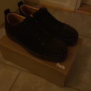 Svarta sneakers med nitar från Christian Louboutin - Snygga svarta sneakers från Christian Louboutin med coola nitar över hela ovandelen. Skorna har en klassisk snörning och en stilren design som sticker ut. Perfekta för dig som vill ha något unikt och trendigt.