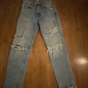 Blå slitna jeans - Säljer ett par blå jeans med slitningar på framsidan. De har en hög midja och en straight passform. Perfekta för en avslappnad stil. 