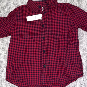 Röd och svart rutig skjorta från Lindex - Säljer en cool röd och svart rutig skjorta från Lindex för barn. Skjortan har långa ärmar och knappar framtill. Perfekt för en stilren look! Ordinarie priset är 200kr och den är aldrig använd med prislapp darför kommer jag att sälja den för hälften av priset!