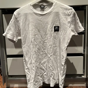 Vit t-shirt från Stone Island - Säljer en vit t-shirt från Stone Island med en liten logga på bröstet. Passar bra till både jeans och shorts. 🏷️