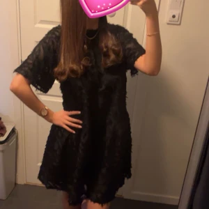 Svart klänning med textur - Snygg svart klänning med korta ärmar och en unik textur. Klänningen har en knytning i ryggen, vilket ger en elegant touch. Perfekt för en stilren look. Endast använt en gång.