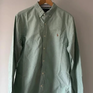 Grön skjorta från Ralph Lauren - Snygg grön skjorta från Ralph Lauren i slim fit. Skjortan har långa ärmar och knappar framtill. Den är broderad med den klassiska logotypen på bröstet. Perfekt för en stilren look.