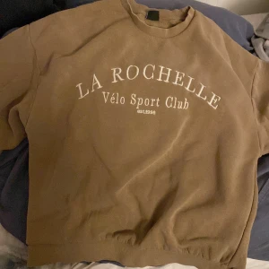 brun tjocktröja med text - brun tjocktröja från gina tricot. tycker den är lite konstigt sydd på vissa ställen men syns inte om man inte tittar efter det. små fläckar på baksidan av en ärm men syns inte mycket i de flesta ljusen