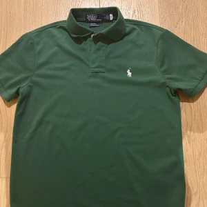 Grön pikétröja från Ralph Lauren - Säljer en snygg grön pikétröja från Ralph Lauren med vit broderad logga på bröstet. Tröjan har korta ärmar och en klassisk krage. Perfekt för en varm sommardag. Skriv om ni har funderingar!