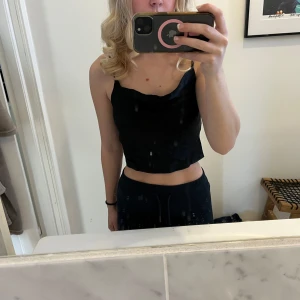 Svart satinlinne från Zara - Säljer ett elegant svart satinlinne från Zara. Linnet har smala axelband och en v-ringad design som ger en stilren look. Perfekt för att klä upp eller ner beroende på tillfälle.