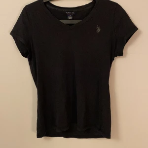 Svart t-shirt från U.S. Polo Assn. - Säljer en svart t-shirt från U.S. Polo Assn. i 100% bomull. T-shirten har en v-ringning och korta ärmar med en liten broderad logotyp på bröstet. Perfekt för en stilren och bekväm look.