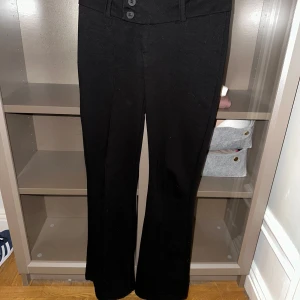 Svarta kostymbyxor - Snygga svarta kostymbyxor med hög midja och bootcut-stil. Byxorna har knappar framtill och är perfekta för en stilren look. Low waist 