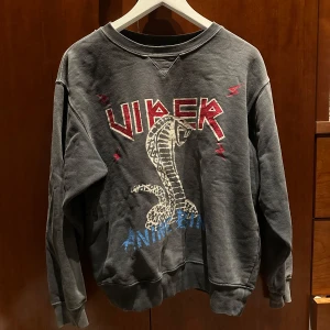 Grå sweatshirt från Anine Bing - Säljer en cool grå sweatshirt från Anine Bing med ett stort tryck av en orm och texten 'Viper' i rött och blått. Tröjan har långa ärmar och en avslappnad passform. Perfekt för en casual look. Den är superskön och i mycket bra skick. Mycket cool och annurlunda och stor i storleken. Skriv för fler bilder🫶🏽