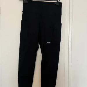 Svarta leggings från SOC - Snygga svarta leggings från Stadium med praktiska sidofickor. Perfekta för träning som håller dig torr och bekväm. Ett måste när man tränar! Stilren design ❤️