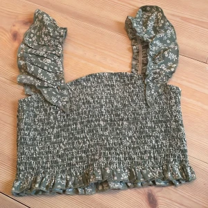 Grön blommig topp med volangärmar - Säljer en superfin grön topp med blommigt mönster och volangdetaljer på axlarna. Toppen är smockad och har en söt volangkant längst ner. Köpt på shein och har knappt använts🩷