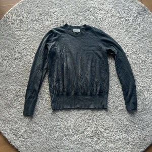 Mörkgrå tröja med knappar - Säljer en stilren mörkgrå tröja med långa ärmar och dekorativa knappar vid ärmsluten. Perfekt för både vardag och lite finare tillfällen. Tröjan är i bra skick och har en skön passform. Passar perfekt till höst- och vintergarderoben!