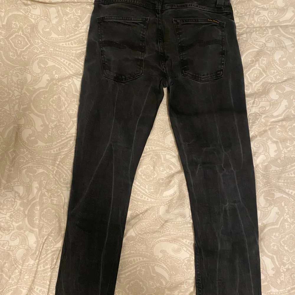 Säljer ett par svarta jeans från Nudie Jeans i storlek 31/34. De har en klassisk femficksdesign med knappar i gylfen. Jeansen är i bra skick och passar perfekt för både vardag och fest. De är tillverkade i slitstarkt denim och har en snygg, mörk tvätt. Modell Grim Tim, nypris 1600kr.. Jeans & Byxor.