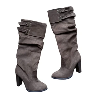 Bruna mockastövlar med klack 36 - Snygga bruna stövlar i mocka med hög klack och coola spänndetaljer upptill. Perfekta för höst, dessa stövlar ger en chic touch till vilken outfit som helst. De har en slouchy design som ger en avslappnad men stilren look.