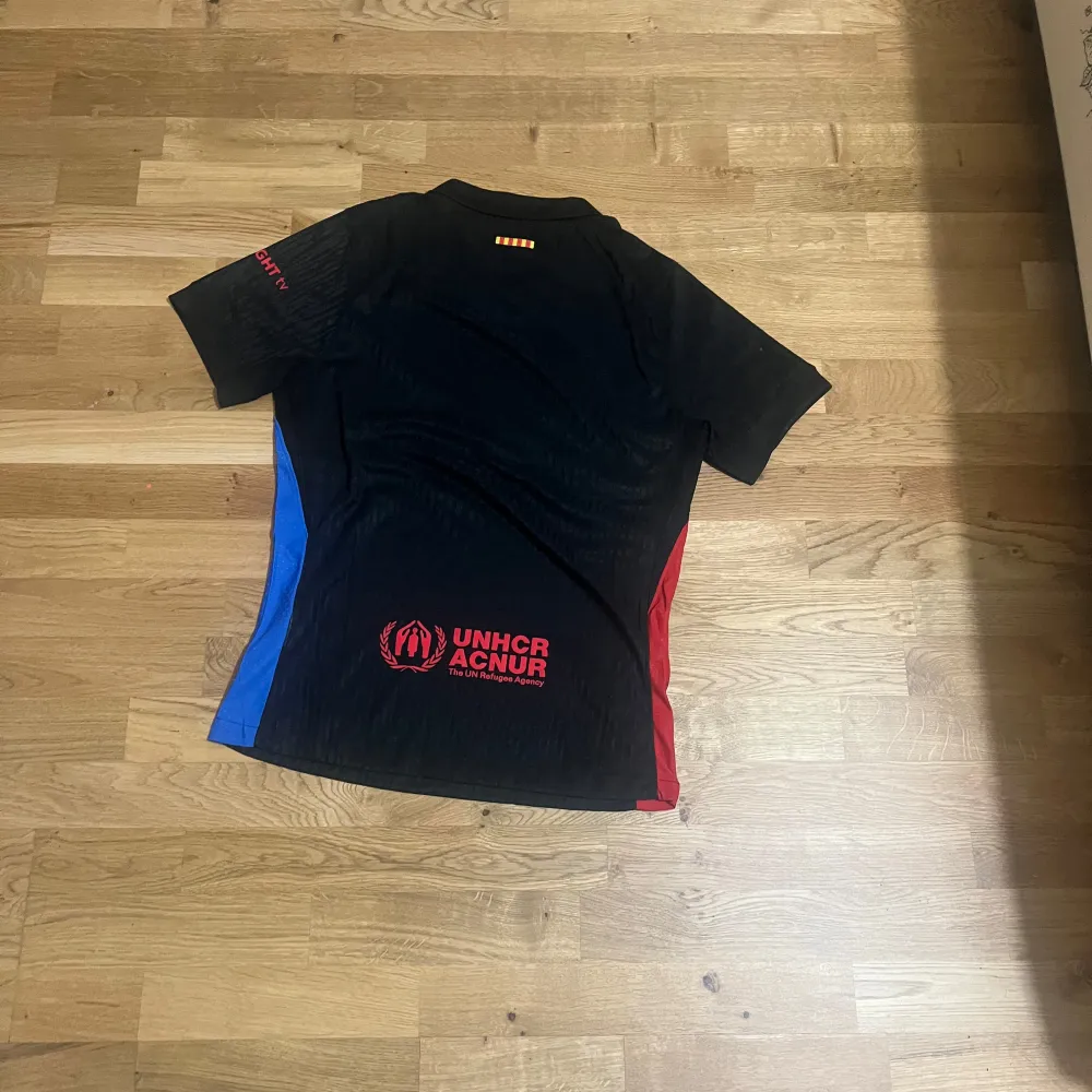 Säljer en svart fotbollströja från Nike med korta ärmar. Tröjan har en röd och blå rand på sidorna och en Spotify-logga på framsidan. Perfekt för fotbollsfans! 🖤🔴🔵. T-shirts.