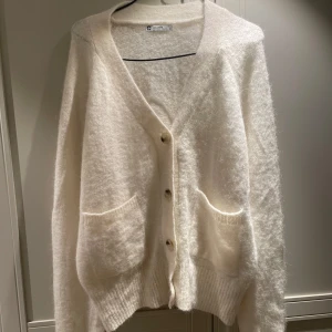 Vit stickad kofta i alpackablandning - Mysig vit kofta i alpackablandning. Den har en v-ringad design med knappar framtill och två praktiska fickor. Perfekt för kyliga dagar.