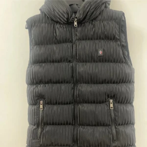 Svart dunväst med dragkedja - Säljer en snygg svart dunväst med dragkedja framtill. Västen har en quiltad design och två praktiska fickor med dragkedjor. Perfekt för höst och vår när du vill hålla dig varm men ändå se stilren ut. Passar både till vardags och lite finare tillfällen.