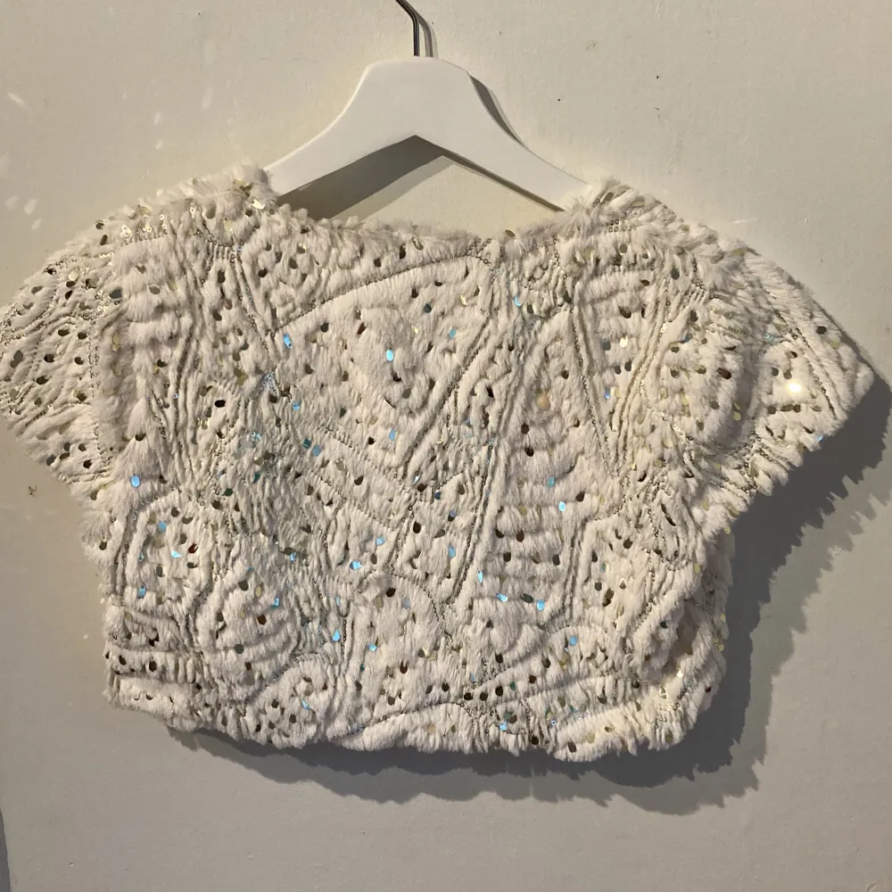 Säljer en superfin vit bolerotopp från Lindex Kids. Den är täckt med glittrande paljetter. Perfekt för festliga tillfällen! Toppen är kortärmad och har en öppen design framtill.. Neuletakit & Villapaidat.