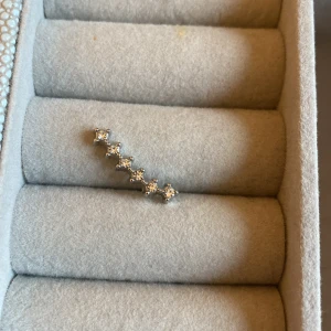 Silverörhänge med glittrande stenar - Snyggt silverörhänge med en rad av glittrande stenar som ger en elegant touch. Perfekt för både vardag och fest. Örhänget har en modern design med en rak linje av små fyrkantiga stenar. 