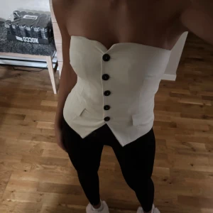 Korsett med knappar - Snygg beige/vit korsett, den har svarta knappar framtill och är axelbandslös. 