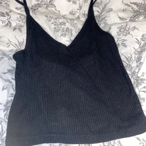 Svart ribbad linnetopp - Säljer en snygg svart ribbad linnetopp med smala axelband och v-ringning. Perfekt för sommardagar eller som ett lager under en jacka. Toppen är i bra skick. Lappen är bortklippt så vet ej vart den kommer ifrån men skulle gissa att den är i storlek XS