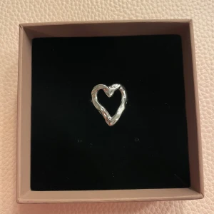 Silver ring hjärta  - Säljer en superfin silverfärgad ring i form av ett hjärta. Den har en modern och stilren design med en öppen justerbar baksida. . Passar både till vardags och fest! Helt ny!