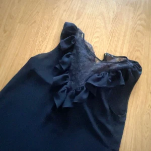 Mörkblå ärmlös blus med spetsdetaljer - Snygg mörkblå blus i ett ärmlöst snitt. Den har en vacker spetsdetalj vid halsen och volanger. Perfekt för både fest och vardag! Det finns ingen lapp kvar så vet inte vart den är ifrån eller vilken storlek det är men enligt mig så tycker jag Xs/S. Kommer inte till användning 