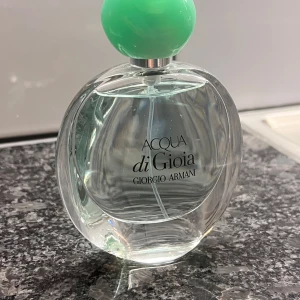 Acqua di Gioia från Giorgio Armani - Säljer en elegant och fräsch parfymflaska av Acqua di Gioia från Giorgio Armani. Flaskan är genomskinlig med en rund form och har en stilren, mintgrön kork. Perfekt för dig som älskar en fräsch och naturlig doft. Passar både till vardags och speciella tillfällen.