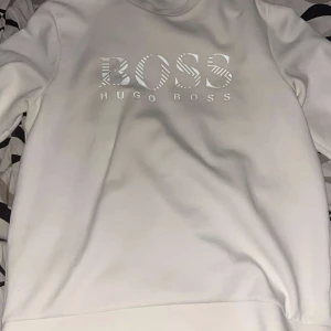Hugo boss tröja vit - Säljer en stilren vit tröja från Hugo Boss i storlek L. Tröjan har ett stort BOSS-tryck på framsidan och är perfekt för en avslappnad men snygg look. Den är i mycket bra skick och passar perfekt för både vardag och fest. Skön och enkel att matcha med det mesta! 🤍