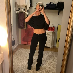 Svarta lågmidjade Manchester byxor - Säljer ett par svarta lågmidjade byxor. De har en snygg guldknapp och dragkedja framtill. Byxorna är tighta upptill och passar perfekt för både vardag och fest. Materialet känns mjukt och bekvämt mot huden. (Köpa secondhand)