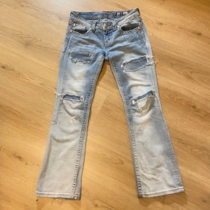 Ljusblå jeans med slitningar från Miss Me - Säljer ett par ljusblå jeans från Miss Me i storlek 28. De är i fint skick. Midjemåttet är 39 cm och innerbensmåttet är 75 cm