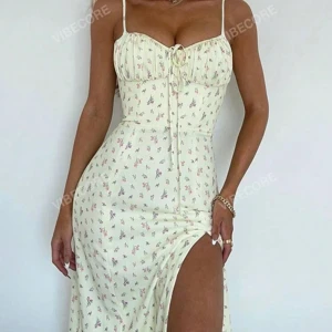 Blommig klänning med slits - Superfin blommig klänning i ljus färg med smala axelband och en söt knytning framtill. Den har en smickrande passform och en slits som ger en extra touch. Perfekt för sommarens alla fester!