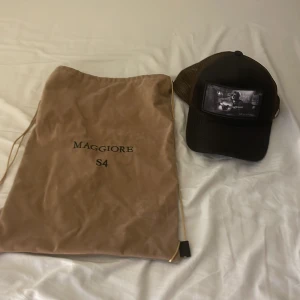 Svart keps med nätpaneler - Säljer en cool svart keps från Maggiore med nätpaneler för extra ventilation. Den har en justerbar rem baktill och en snygg patch framtill. Perfekt för sommarens alla äventyr! 🧢 Låda till kepsen kommer med!