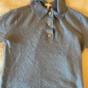 Blå kortärmad tröja från H&M - Säljer en superfin blå kortärmad tröja från H&M. Den har en klassisk pikékrage och tre glittriga knappar framtill som ger en extra touch. Perfekt för både vardag och festliga tillfällen. Materialet känns mjukt och bekvämt. Passar perfekt till jeans eller kjol!
